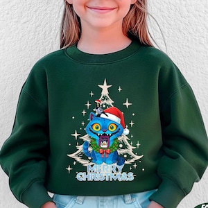 May include: Forest green sweatshirt featuring a blue cat wearing a Santa hat and a Christmas wreath. The cat is in front of a Christmas tree with the words "MERRY CHRISTMAS" below.