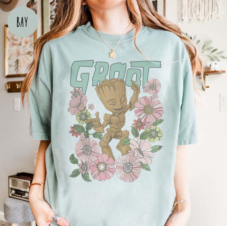 May include: A light blue t-shirt featuring a floral design and a graphic of Groot from Guardians of the Galaxy. The text "Groot" is printed in large letters above the graphic.