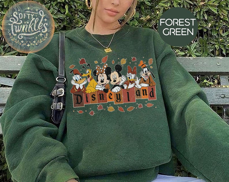 May include: A forest green sweatshirt with a graphic print of Mickey Mouse and friends in front of a sign that says "Disneyland".