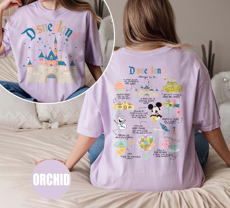 Może przedstawiać: Fioletowy T-shirt z nadrukiem graficznym zamku Disneylandu i tekstem "Disneyland" z przodu. Z tyłu T-shirt ma nadrukowane grafiki atrakcji Disneylandu i tekst "Disneyland rzeczy do zrobienia".