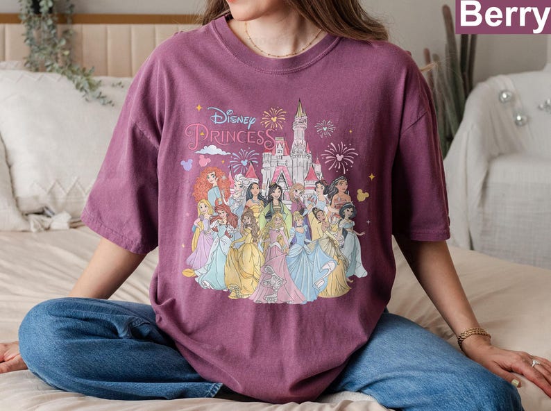 May include: A purple t-shirt with a graphic of Disney princesses in front of Cinderella's castle. The text "Disney Princess" is printed on the shirt.