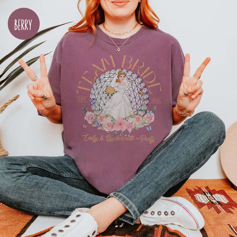 May include: Purple t-shirt with the text "Team Bride" and a graphic of a bride in front of a sphere. The text "2023" and "Est. 2021" are on either side of the graphic. The text "Emily & Bachelorette Party" is at the bottom of the graphic.