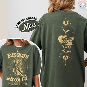 May include: Moss green t-shirt with gold graphic designs on the front and back. The front features text that reads "BASGIATH WAR COLLEGE DRAGON RIDER" with a dragon illustration. The back has a vertical design with bat and cloud illustrations.