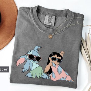May include: Gray t-shirt with a graphic of Stitch and Lilo wearing sunglasses. The shirt has the text "COMFORT COLORS" and "S - P - CH" printed on the tag.