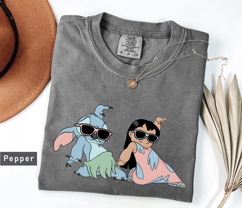 May include: Gray t-shirt with a graphic of Stitch and Lilo wearing sunglasses. The shirt has the text "COMFORT COLORS" and "S - P - CH" printed on the tag.