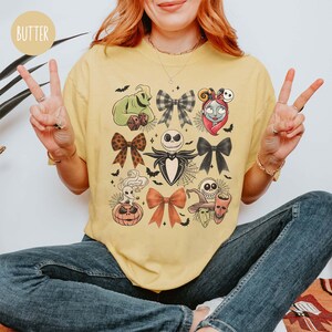 May include: A yellow t-shirt with a design featuring characters from The Nightmare Before Christmas. The design includes images of bows, Jack Skellington, and other characters. The word "BUTTER" is printed on the top left corner of the shirt.