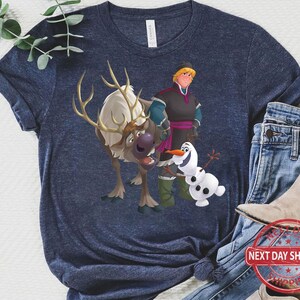 May include: A navy blue t-shirt featuring a cartoon image of Olaf, Kristoff, and Sven from the film Frozen. The characters are smiling and standing together.
