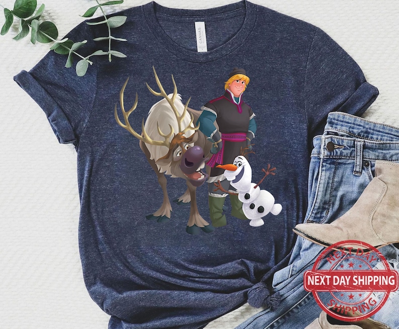 May include: A navy blue t-shirt featuring a cartoon image of Olaf, Kristoff, and Sven from the film Frozen. The characters are smiling and standing together.