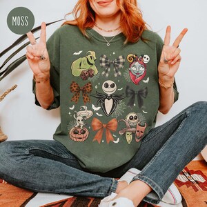May include: A moss green sweatshirt with various cartoon character designs, including Jack Skellington, Sally, and Oogie Boogie. The designs are arranged in a pattern of bows and character faces. The word "MOSS" is in a green circle in the upper left corner.