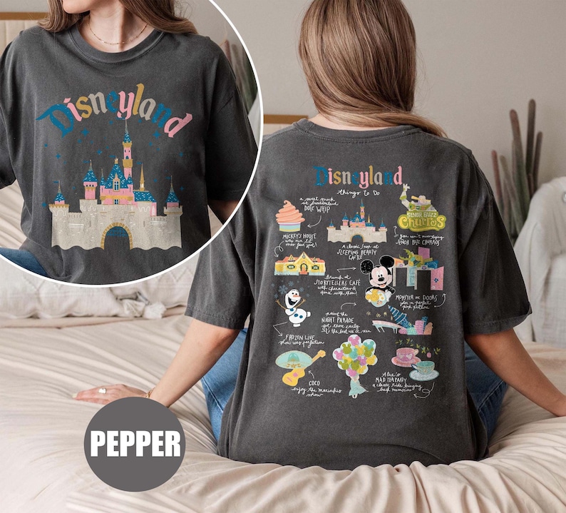Może przedstawiać: Czarny T-shirt z grafiką w stylu vintage zamku Śpiącej Kr&oacute;lewny z Disneylandu z przodu i listą rzeczy do zrobienia w Disneylandzie z tyłu. Tekst z tyłu zawiera "Disneyland Things to Do" i wymienia atrakcje takie jak "Haunted Mansion", "Jungle Cruise" i "Space Mountain".