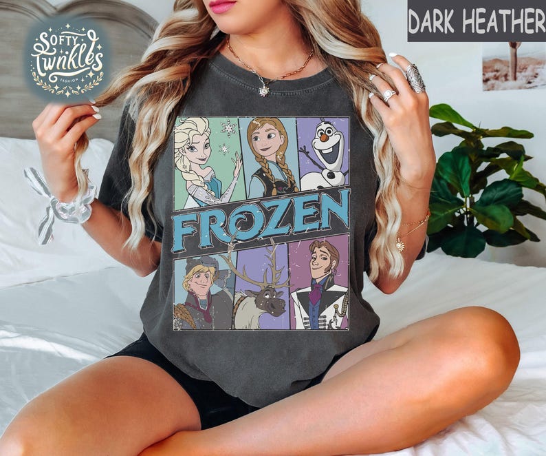 May include: A dark heather grey t-shirt with a vintage-style graphic of characters from the movie Frozen. The graphic features Elsa, Anna, Olaf, Kristoff, and Sven. The text "FROZEN" is printed in blue letters.