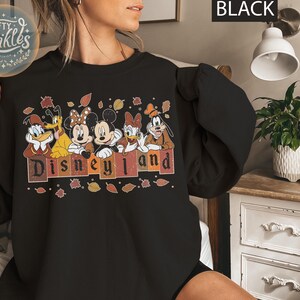 May include: Black sweatshirt with a graphic of Mickey Mouse and friends in front of a fall-themed Disneyland sign. The text "Disneyland" is in a vintage font.