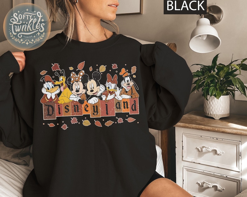 May include: Black sweatshirt with a graphic of Mickey Mouse and friends in front of a fall-themed Disneyland sign. The text "Disneyland" is in a vintage font.