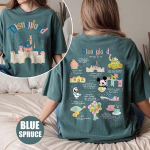 Może przedstawiać: Koszulka w kolorze turkusowym z nadrukiem graficznym Disneylandu. Prz&oacute;d koszulki przedstawia duży obraz zamku Śpiącej Kr&oacute;lewny. Tył koszulki zawiera listę rzeczy do zrobienia w Disneylandzie, w tym dom Myszki Miki, stoisko z churrosami i przejażdżkę o nazwie "Monsters Inc. Laugh Floor".