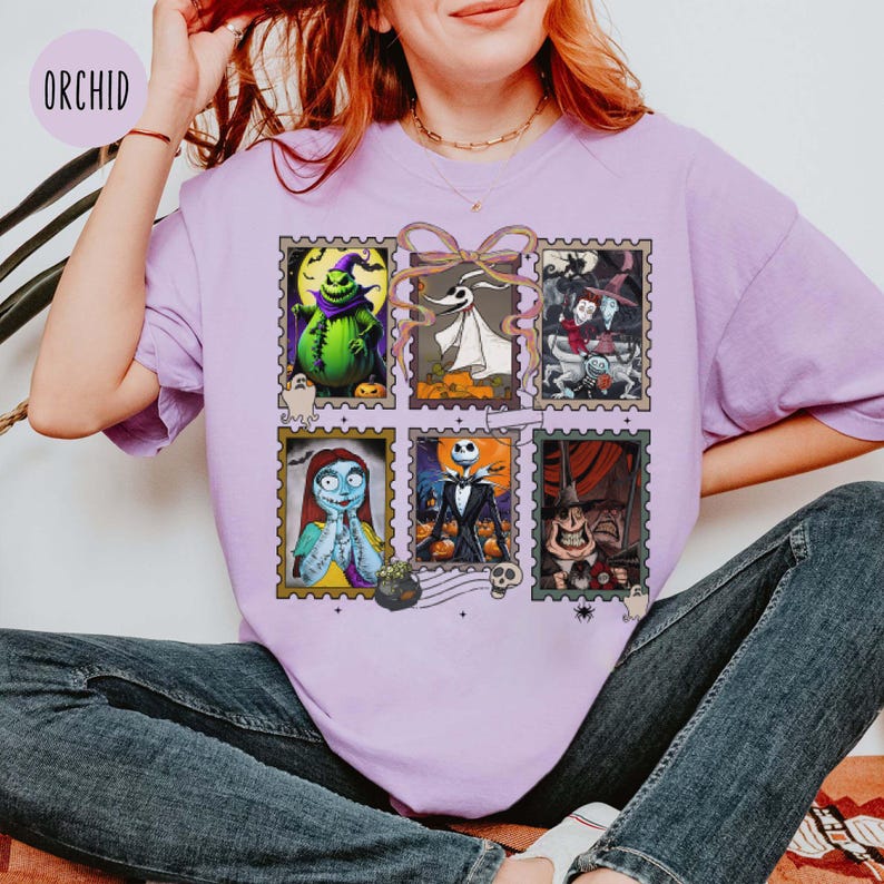 May include: A light purple t-shirt featuring six postage stamp-style images of characters from a movie. The images include a green character, a ghost, a witch, a character with blue skin, a character in a tuxedo, and a character with a large grin.