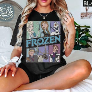 May include: Black t-shirt with a vintage-style graphic of characters from the Disney movie Frozen. The graphic features Elsa, Anna, Kristoff, Olaf, and Sven. The text "FROZEN" is printed in large, bold letters.