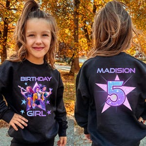 May include: Black sweatshirt with a colorful graphic on the front that says "BIRTHDAY GIRL" and features a cartoon image of three girls. The back of the sweatshirt has the name "MADISION" and the number "5" inside a star.