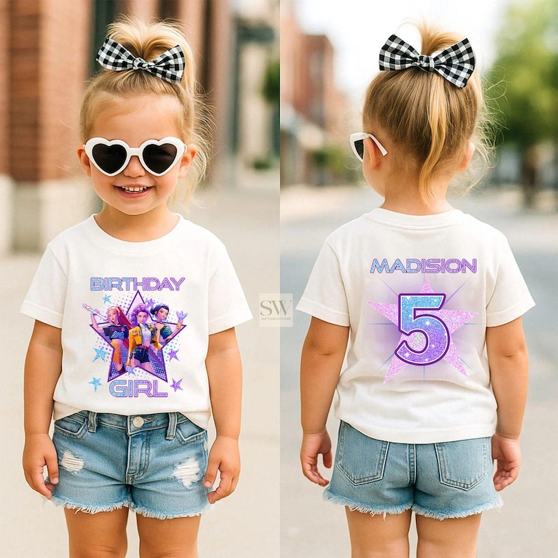 May include: A white t-shirt with a graphic design featuring the text "BIRTHDAY GIRL" and a star design with three cartoon characters. The back of the shirt has the name "MADISON" and the number "5". The girl is wearing denim shorts and heart-shaped sunglasses.