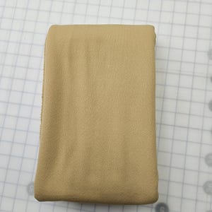 May include: Folded tan fabric, likely a textile or material for crafting or sewing. The fabric has a slightly textured surface and appears to be a solid color. The edges are neatly folded, suggesting a finished product or a piece ready for use.