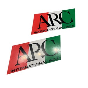 Könnte beinhalten: Zwei Aufkleber mit dem Text "ARC INTERNATIONAL INC." in schwarzen Buchstaben auf weißem Hintergrund. Die Aufkleber sind rautenförmig und haben die Farben der italienischen Flagge: Rot, Weiß und Grün.