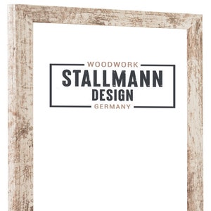 Può includere: Una cornice per foto in legno bianco con una finitura usurata. La cornice ha un'etichetta nera con il testo "WOODWORK STALLMANN DESIGN GERMANY".