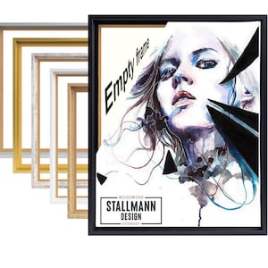 Op de afbeelding: Een zwart omlijst kunstwerk met een aquarelportret van een vrouw, met de woorden "Empty frame" in de linkerbovenhoek. Het kunstwerk staat naast een stapel verschillende gekleurde lijsten, waaronder zilveren, gouden, witte en houtkleurige lijsten. Het kunstwerk heeft de tekst "WOODWORK - STALLMANN DESIGN - GERMANY".