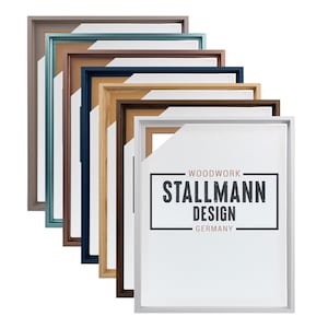 Può includere: Una collezione di cornici rettangolari in vari colori, tra cui marrone, verde acqua, blu navy e bianco. Le cornici sono impilate ad angolo, rivelando il logo "STALLMANN DESIGN GERMANY".