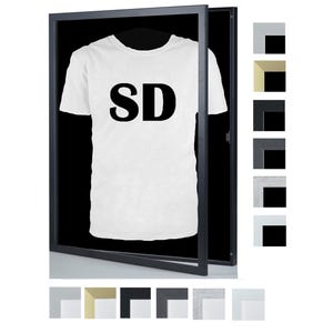 Op de afbeelding: Wit t-shirt met de zwarte letters "SD", gepresenteerd in een zwart frame. Het frame is open en toont het t-shirt op een hanger. Verschillende framekleuropties worden rechts en onder de hoofdafbeelding weergegeven.