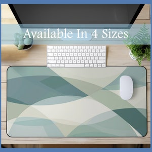 May include: A desk mat with a geometric pattern of overlapping white and green curves. The mat is on a wooden desk with a keyboard, mouse, and two potted plants. The text "Available In 4 Sizes" is at the top of the image.