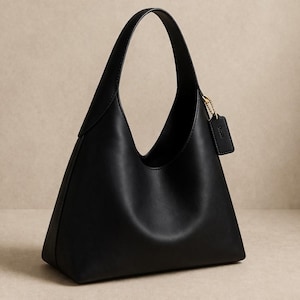 May include: A black leather handbag with a unique, triangular shape. The bag has a single handle and a small, rectangular tag attached with a gold-colored chain. The bag's design is minimalist and modern, suitable for everyday use.