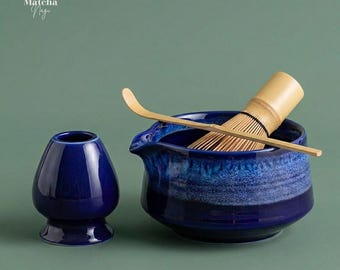 May include: A matcha tea set featuring a deep blue ceramic bowl, a whisk, and a bamboo scoop. The set includes a smaller, matching blue ceramic container. The text "Matcha Nagi" is in the upper left corner.