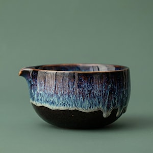 May include: A ceramic tea pitcher with a dark blue and black glaze. The pitcher has a spout and a rounded body. The glaze has a dripped effect, with streaks of blue and white. The bottom of the pitcher is black.
