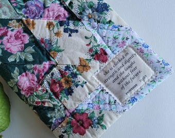 Puede incluir: Un artículo de tela acolchada con un estampado floral en tonos rosa, morado, verde y crema. Un pequeño parche con el texto "She is clothed in strength and dignity and she laughs without fear of the future. Proverbs 31:25."