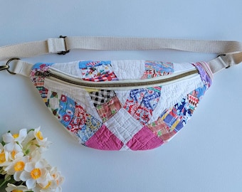 Puede incluir: Una riñonera en forma de media luna confeccionada con una colcha de retazos que presenta varios cuadrados de tela coloridos en tonos rosa, azul, rojo y blanco. El bolso incluye una correa ajustable de color beige y una cremallera metálica.