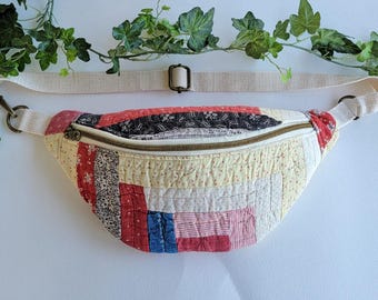 Puede incluir: Riñonera acolchada con correa crema y herrajes bronce. El bolso presenta un diseño patchwork con telas rojas, azules y crema. La cremallera es de color bronce. Un accesorio de moda y práctico.