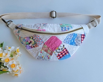 Puede incluir: Una riñonera en forma de media luna confeccionada en tela acolchada con un diseño de patchwork de varios cuadrados coloridos con estampados florales, de cuadros y lisos. El bolso incluye una correa ajustable de lona beige y cremallera metálica.