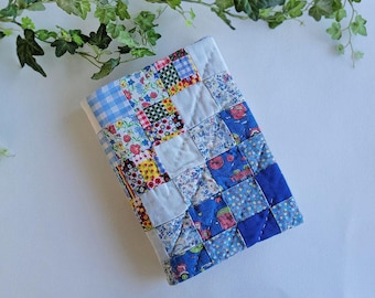 Puede incluir: Un edredón de retazos rectangular con una variedad de patrones de tela, incluyendo cuadrados florales, cuadros y azules lisos. El edredón es principalmente azul, blanco y rojo, con una textura acolchada.