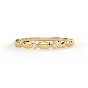 May include: A gold ring featuring a repeating pattern of oval links, each linked by a small, clear gemstone. The ring's polished surface reflects light, and the gemstones provide a subtle sparkle. The ring is displayed against a white backdrop.