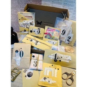 May include: A collection of vintage-style ephemera, including numbered tags, paper packets, and decorative elements. The items are arranged in a box and on a surface, with a butterfly logo and the text "CRAZY JOURNALIST".