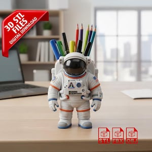May include: A white astronaut-shaped desk organizer holding pens and pencils. The astronaut has blue and orange accents, a black visor, and a small American flag on the shoulder. The image includes the text "3D STL FILES DIGITAL DOWNLOAD".
