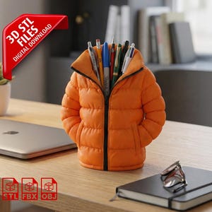 May include: Orange puffer jacket-shaped pen holder filled with pens and pencils. The pen holder is on a wooden desk next to a laptop, a succulent plant, and a notebook. A red banner reads "3D STL FILES DIGITAL DOWNLOAD".