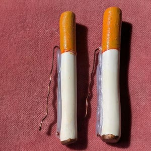 Puede incluir: Dos pinzas para el pelo en forma de cigarrillo, blancas y naranjas, con detalles de alambre de cobre.