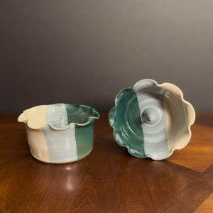 May include: Two handmade ceramic bowls with a scalloped edge. The bowls are glazed in shades of green, blue, and white.