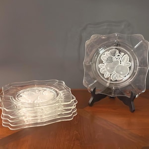 May include: A set of six clear glass square plates with scalloped edges. Each plate features a central frosted glass design depicting a pear and leaves. One plate is displayed upright on a black stand, while the other five are stacked together.