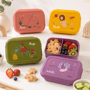 Peut inclure: Quatre boîtes à lunch rectangulaires en plastique rose, jaune, vert olive et violet. Chaque couvercle présente une illustration animale unique et un prénom : Luna, Noah, Hugo ou Juliette. Une boîte violette est ouverte, montrant des biscuits.
