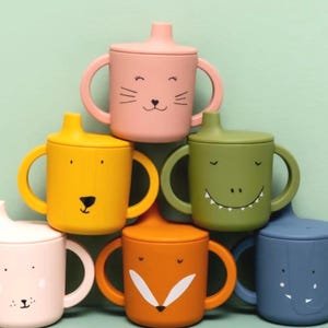 May include: A selection of brightly coloured baby cups, each with a lid and handle. The cups are decorated with animal faces, such as a cat, bear, alligator, fox, and elephant. The cups are in pink, yellow, green, orange, and blue.