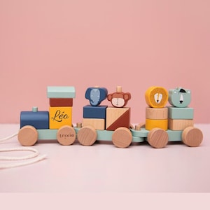 May include: A colourful wooden toy train with animal-shaped blocks. The train is painted in blue, green, yellow, and brown. The blocks feature an elephant, monkey, lion, and bear. The name "Léa" is printed on the side, and the brand name "trixie" is on the wheels.