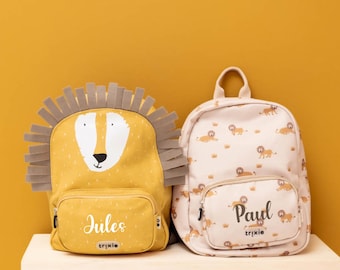 Könnte beinhalten: Zwei Kinderrucksäcke. Einer ist gelb mit einem Löwengesicht-Design und dem Namen "Jules". Der andere ist hellrosa mit einem Löwenmuster und dem Namen "Paul". Beide haben eine kleine Vordertasche und einen oberen Griff.