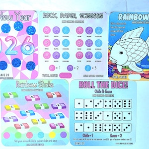 May include: A set of savings challenge cards with different designs. Themes include "Happy New Year 2026", "Rock, Paper, Scissors", "Rainbow Fish", "Rainbow Stacks", and "Roll the Dice!" Each card has unique graphics and instructions for saving money.