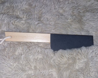 May include: A wooden sanding block with a black sanding surface and a white string attached to the handle.